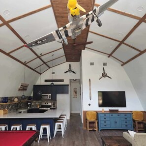 Een moderne keuken met een centraal eiland, een eethoek met barstoelen, een woonkamer met een televisie en een plafondventilator.