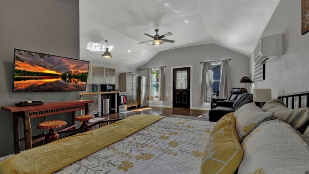 A spacious bedroom with a large bed, a ceiling fan, a flat-screen TV, and a view of the outdoors. - Quonset-Style Cabin & Sunset Patio Near Blue Hole (Wimberley)