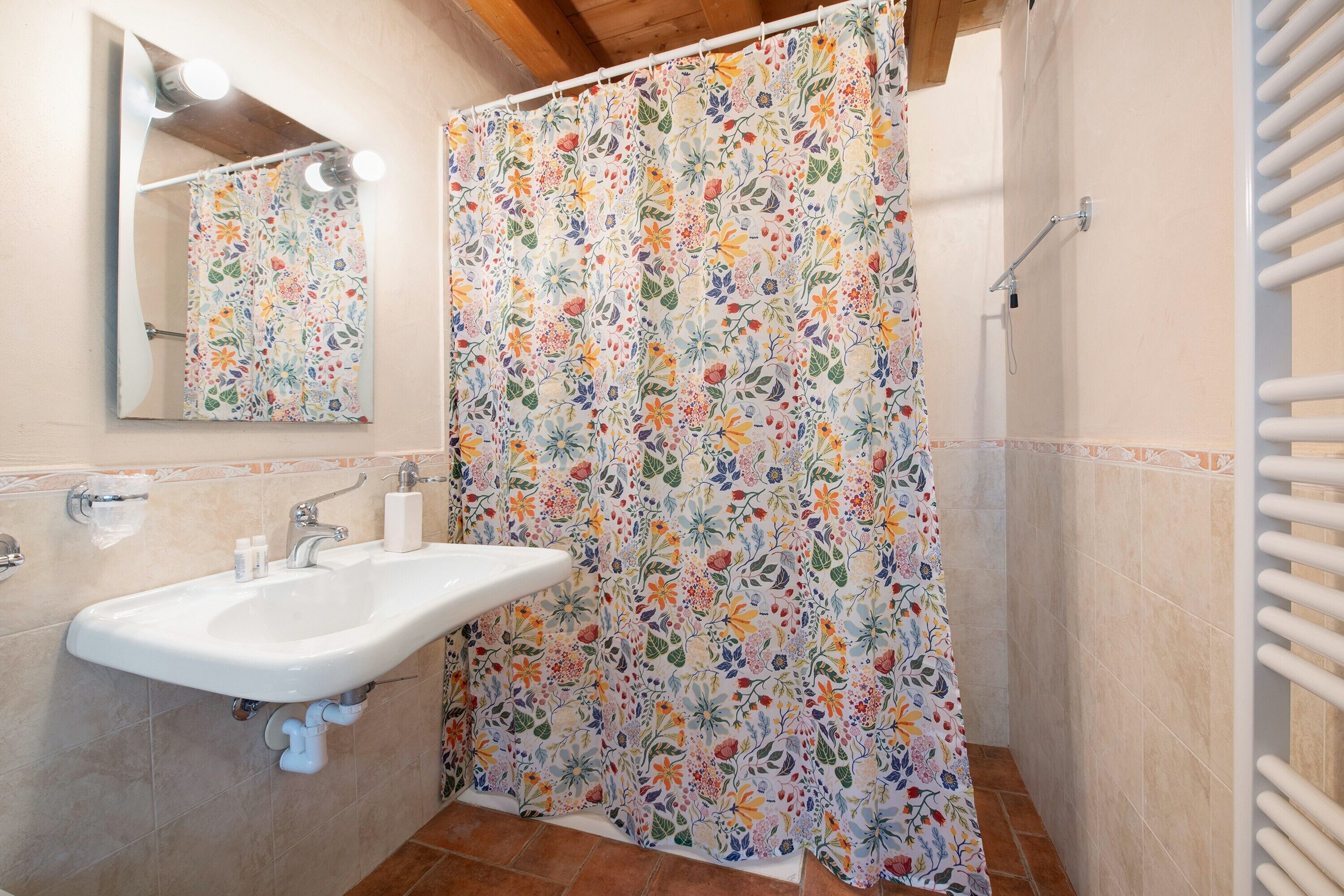 Baño con lavamanos, espejo, cortina de ducha y paredes con azulejos.