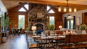 A cozy log cabin interior with a stone fireplace, wooden beams, and a dining area set up for a meal. - Compass Retreat for large groups (Buchanan)