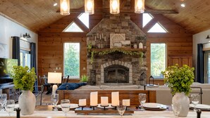 A cozy lodge interior with a stone fireplace, wooden ceiling, and a dining area set for six. - Compass Retreat for large groups (Buchanan)