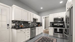 A modern kitchen with white cabinets, stainless steel appliances, and a patterned rug. - Basecamp - 3 miles to DT (Fayetteville)