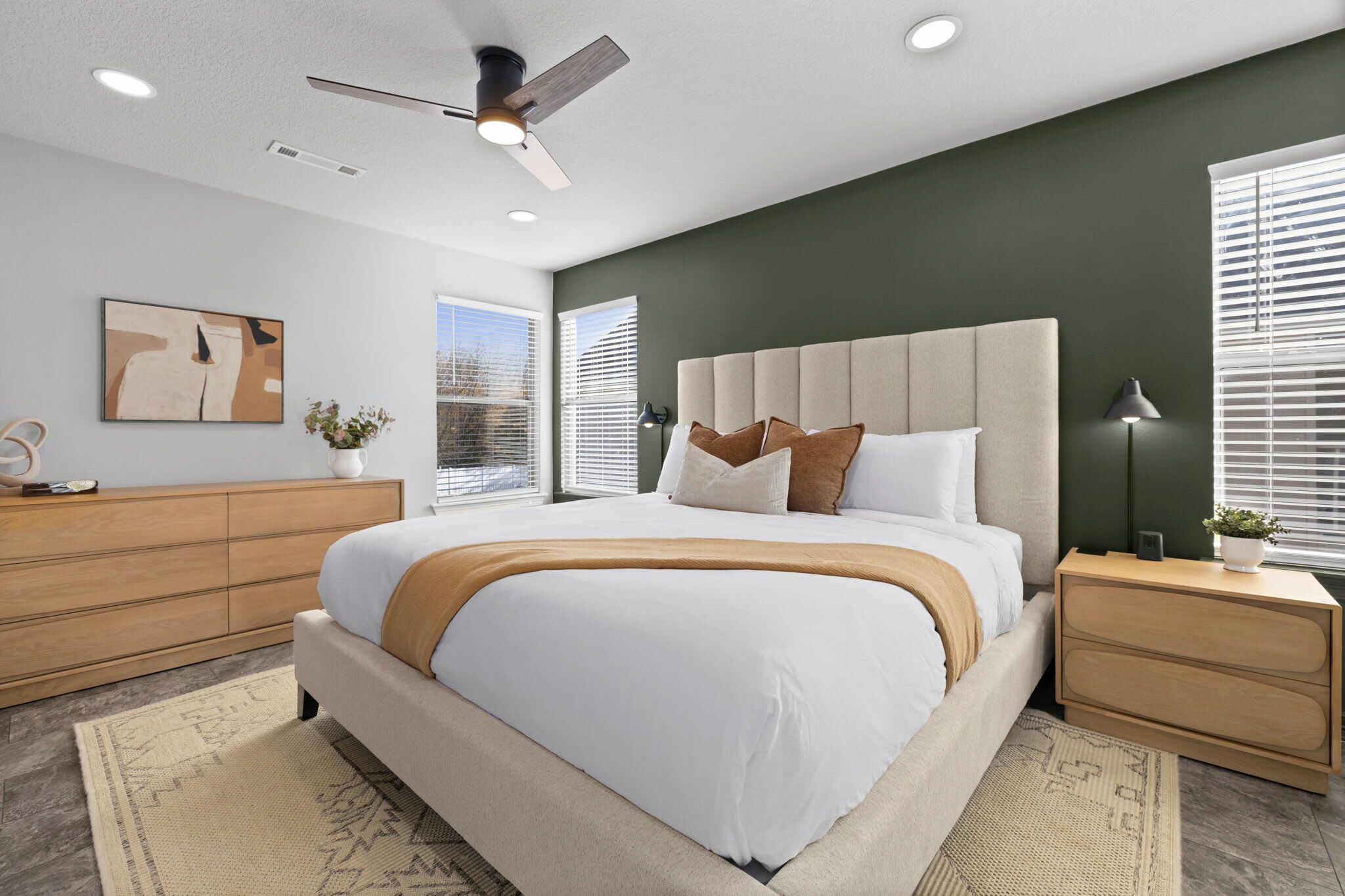 Une chambre moderne avec un grand lit, un ventilateur de plafond, une table de chevet et une fenêtre avec des stores.