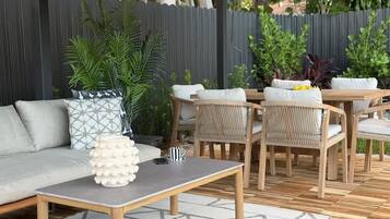 Un área de patio al aire libre con un sofá, una mesa de madera y sillas de mimbre.