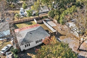 A residential property with a fenced yard, a red-roofed building, and a white house. - Chic 2/2 Cottage Near Downtown & Beaches (Mount Pleasant)