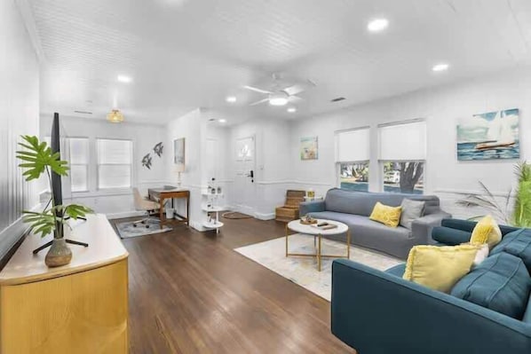 A spacious living room with a large sofa, a coffee table, and a television on a wooden stand. - Chic 2/2 Cottage Near Downtown & Beaches (Mount Pleasant)