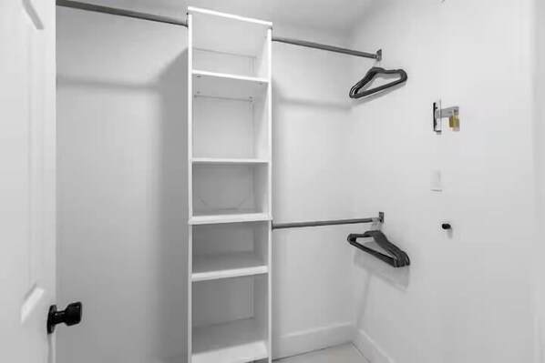 A white closet with a metal rod and hooks for hanging items. - Chic 2/2 Cottage Near Downtown & Beaches (Mount Pleasant)