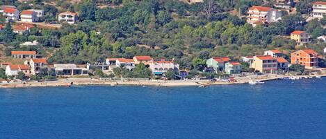 A coastal town with houses along the shoreline, a beach, and a hilly backdrop.