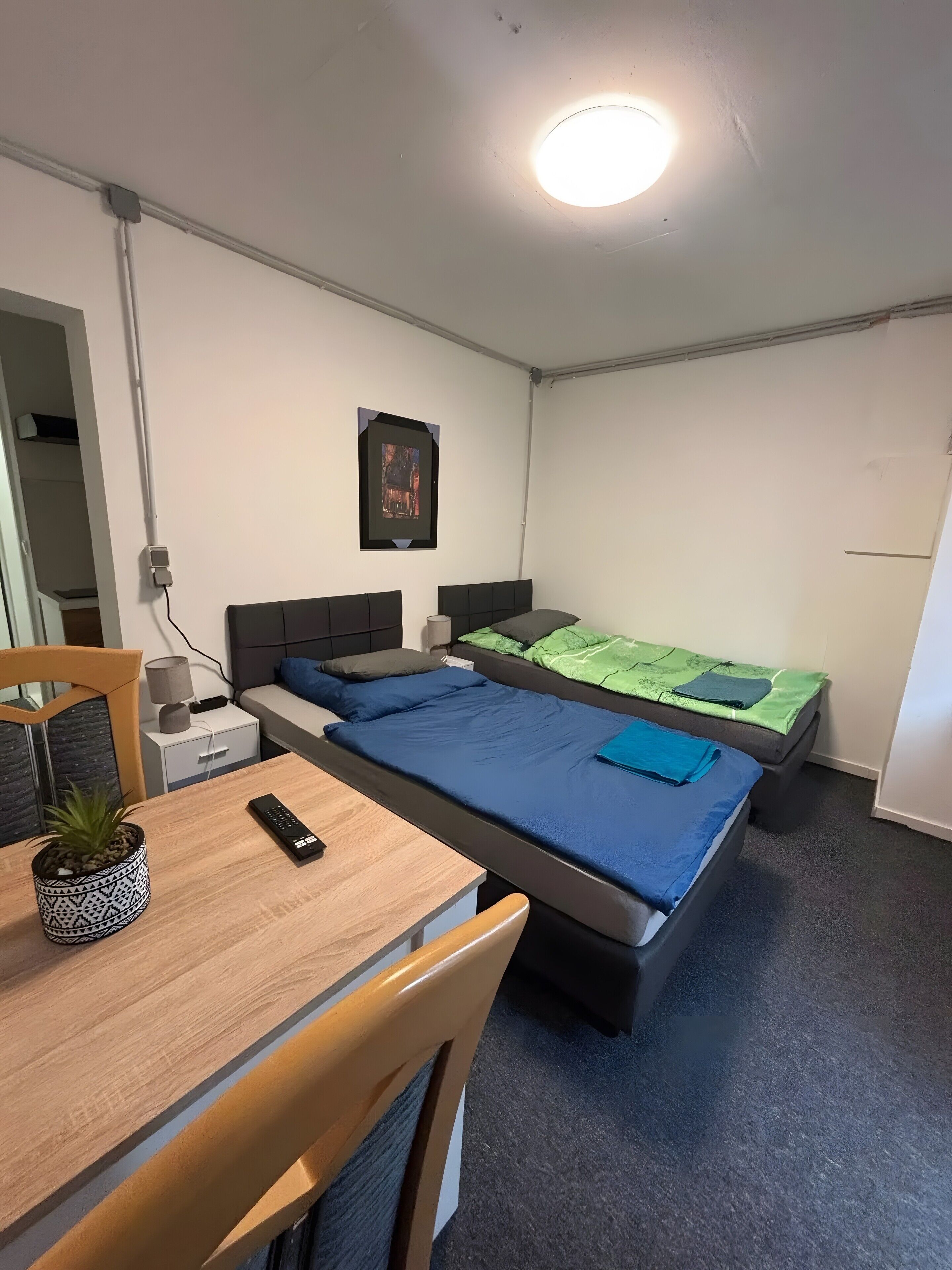Huoneessa on sänky, työpöytä, tuoli, lamppu ja seinälle ripustettu taulu.