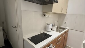 Una cocina compacta con una placa de inducción negra, un hervidor, un lavamanos y armarios de madera.