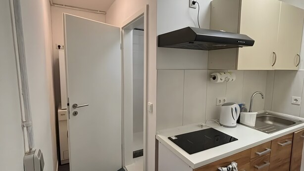Una cocina compacta con encimera blanca, extractor de humos negro y armarios de madera.