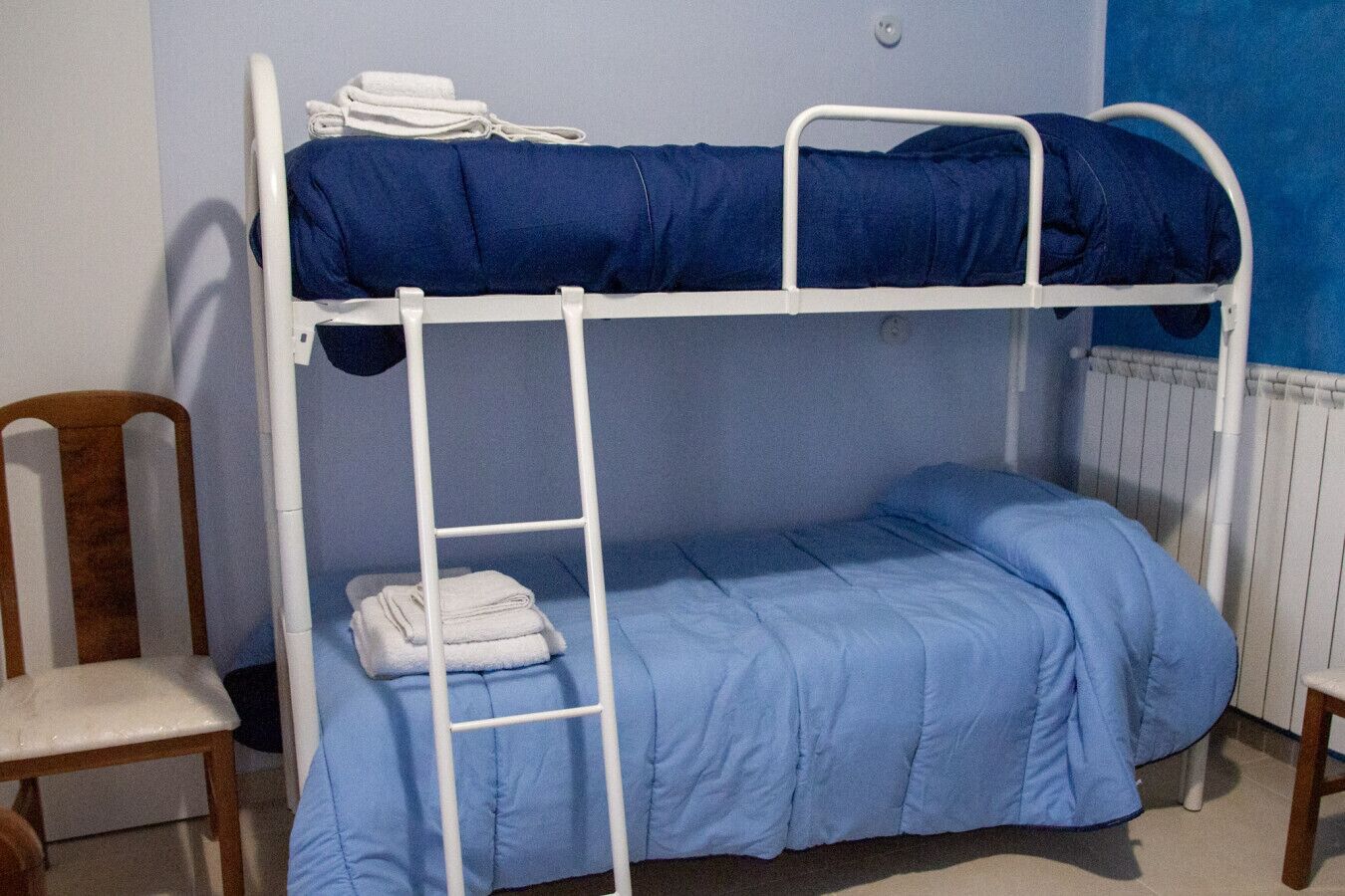 Ein Stockbett mit einer Leiter, einem Stuhl und einem Heizkörper.
