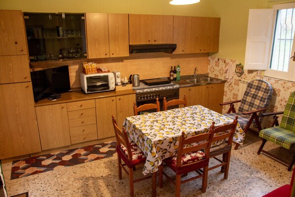 A compact kitchen with wooden cabinets, a microwave, a stove, and a dining table with chairs. - Casa Vacanze Chimenti - Tarsia (Tarsia)