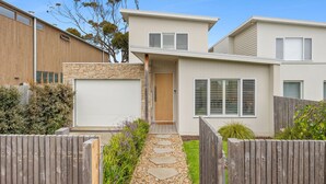Une maison moderne à deux étages, dotée d’une façade en pierre, d’une porte en bois et d’un garage.