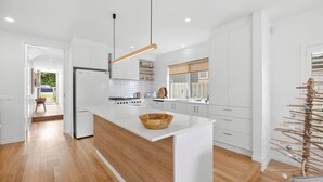 Une cuisine moderne avec des meubles blancs, un îlot central en bois et un luminaire suspendu.