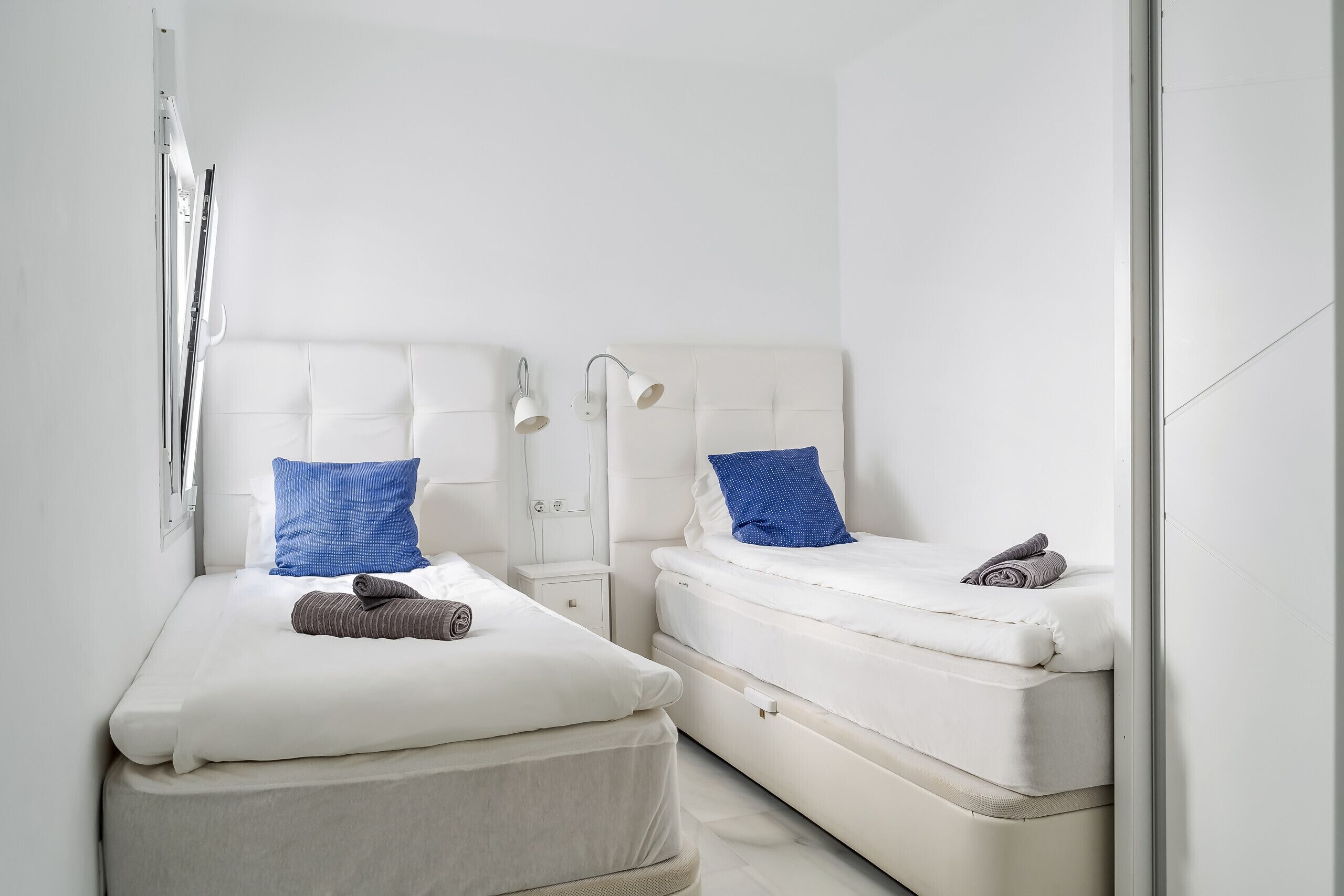 Une chambre à coucher moderne et minimaliste, avec deux lits, chacun doté d’une tête de lit et de tables de chevet.
