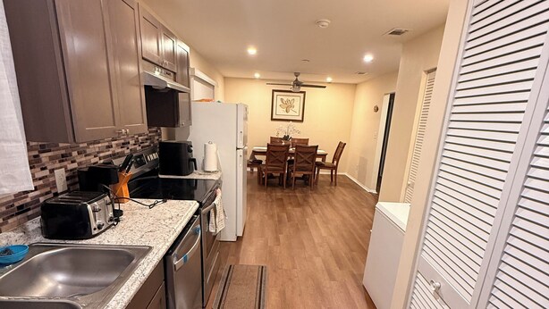 A compact kitchen with a microwave, toaster, and sink. There is a dining area with a table and chairs in the background.