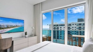 A modern hotel room with a large bed, a TV on the wall, a balcony with a pool view, and a cityscape in the background. - Villa DecoBlu (Miami Beach)