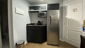 Eine kompakte Küche mit schwarzem Arbeitsplatz, einem Edelstahl-Kühlschrank, einer Mikrowelle und einem Mülleimer.