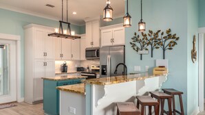 Una cocina moderna con armarios blancos, una isla verde azulada y taburetes de bar.