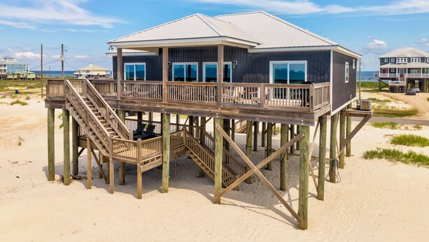 Una casa frente a la playa con una terraza de madera y varias ventanas.