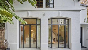 Ein modernes Gebäude mit weiß verputzter Fassade, großen bogenförmigen Glasüren und einem einsehbaren Innenbereich mit Essbereich.