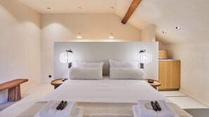 Ein modernes Hotelzimmer mit einem großen Bett, zwei Nachttischen, einer hölzernen Bank, einem kleinen runden Tisch und einem Holzschrank.