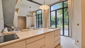 Eine moderne Küche mit einer großen Kochinsel, einem eingebauten Backofen und einem großen Fenster mit Blick auf Grünflächen.