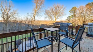 Una terraza de madera con mobiliario exterior, incluyendo sillas y una mesa, con vistas a un paisaje montañoso.