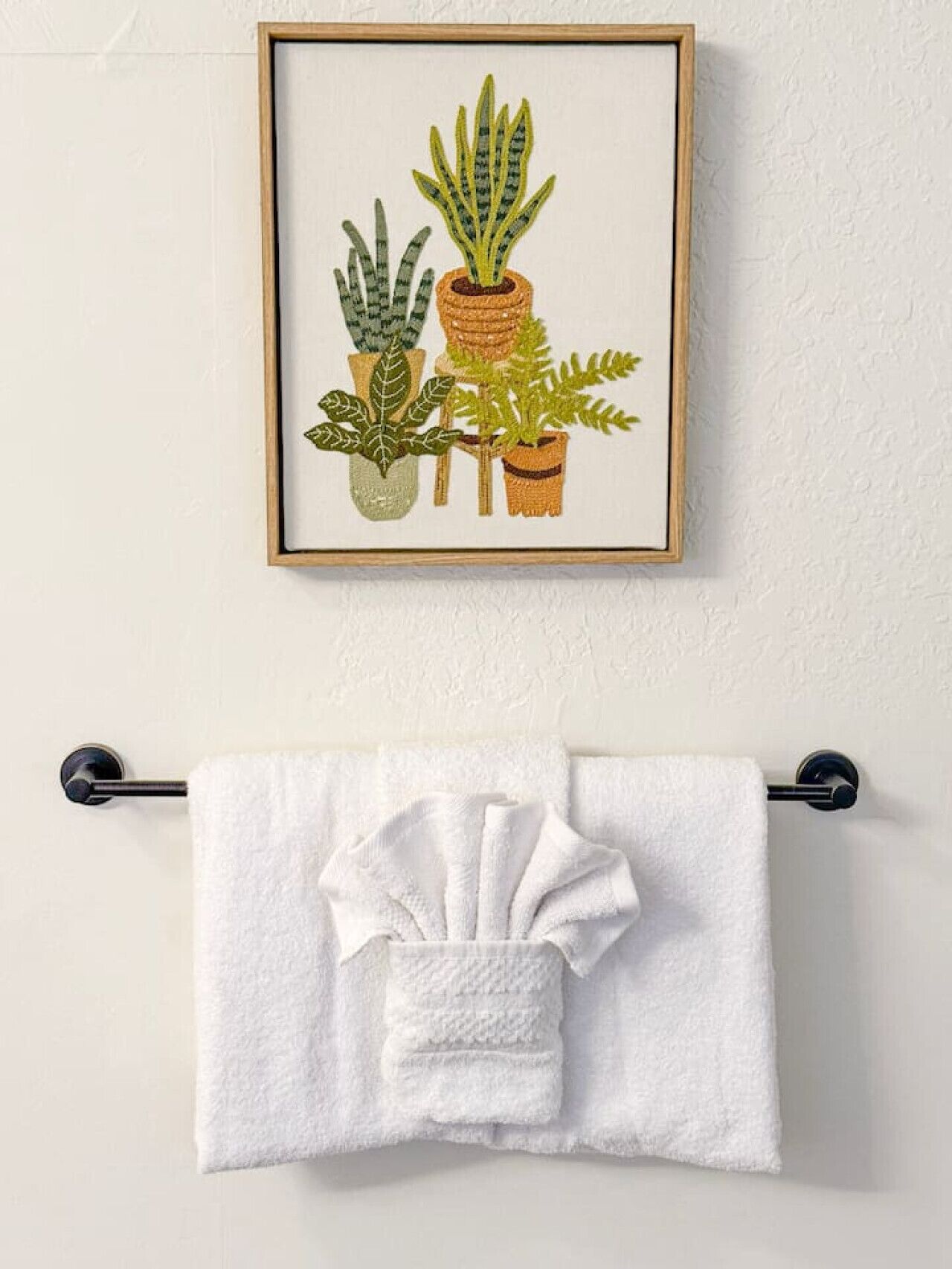 En indrammet illustration af forskellige planter på en væg, med et hvidt håndklæde hængende under.