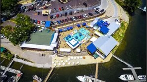 Luchtbeeld van een pand aan het water met een zwembad, een tennisbaan en een steiger met boten.