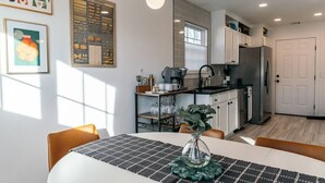 Une cuisine moderne avec des meubles blancs, un réfrigérateur en acier inoxydable et un coin repas avec une table dressée pour deux personnes.