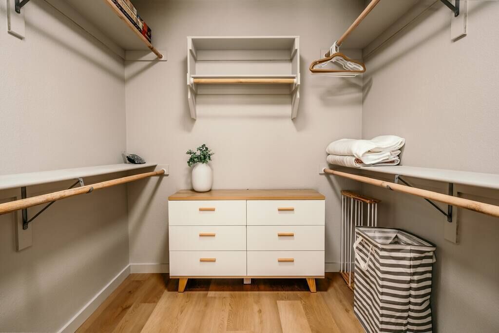 A walk-in closet with wooden shelves, a white dresser, and a striped laundry basket.