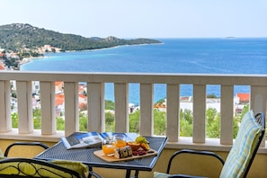 Ein Balkon mit Frühstückstisch, mit Blick auf die Küste, Gebäude und Hügel.