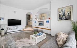 Ein modernes Wohnzimmer mit einem Flachbildfernseher, einer Treppe, die zu einer Küche führt, und einem gerahmten Gemälde an der Wand.