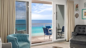 A balcony with a view of the ocean, a blue armchair, a grey sofa, and a small table with chairs.