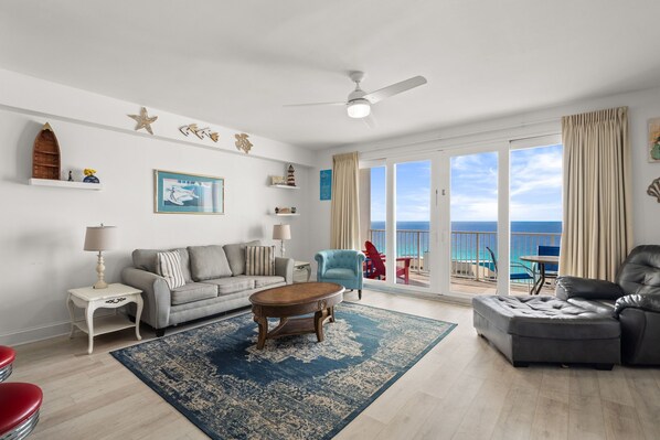 Ein Wohnzimmer mit Sofa, Sessel, Hocker, Couchtisch und Meerblick durch große Fenster.