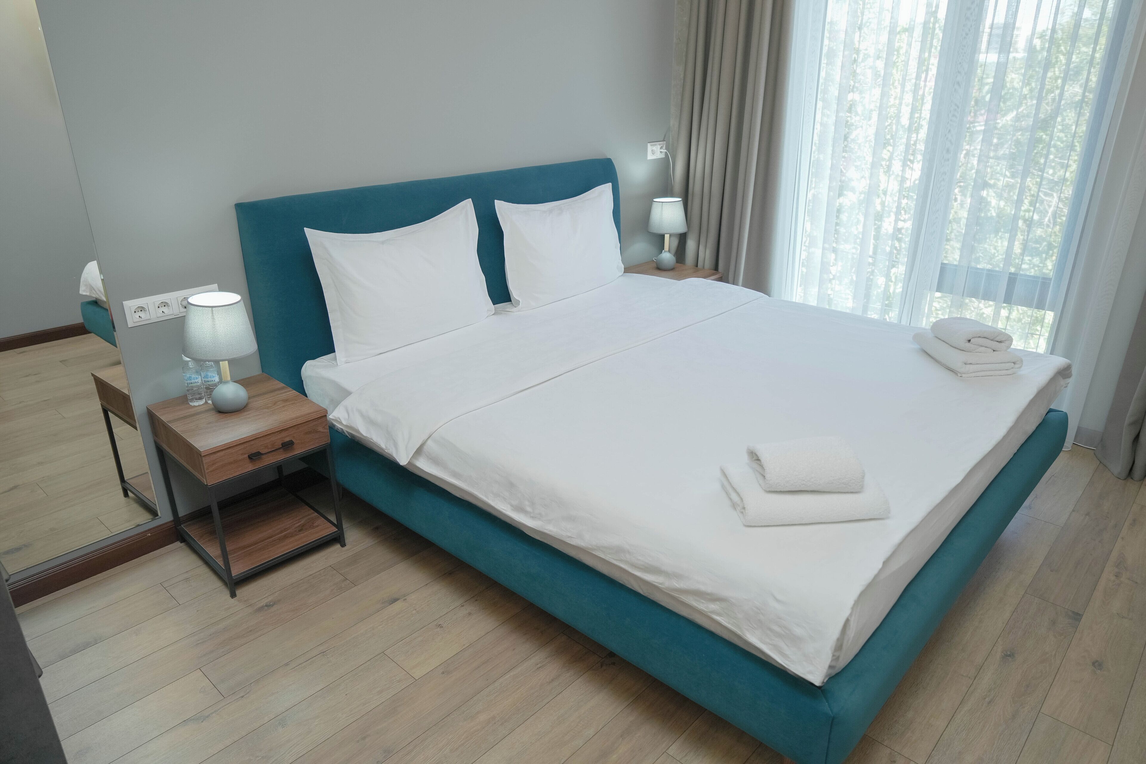 Una cama bien hecha con sábanas blancas y un cabecero color turquesa en una habitación de hotel.