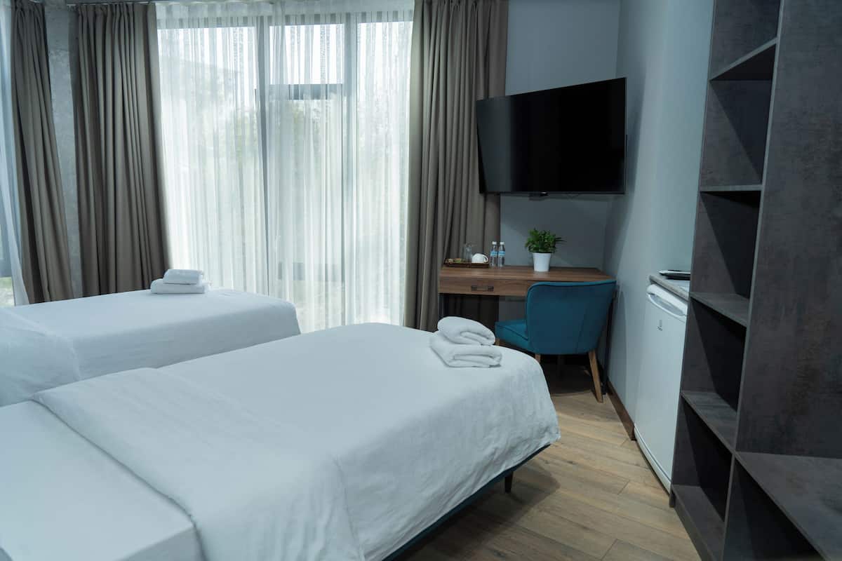 Une chambre d’hôtel avec deux lits, un bureau avec une chaise, une télévision et une armoire.