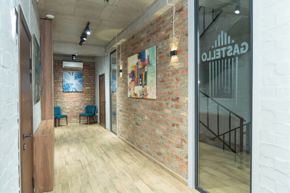 A hallway with a brick wall, wooden floor, and two blue chairs. - Gastello Hotel (Bishkek)