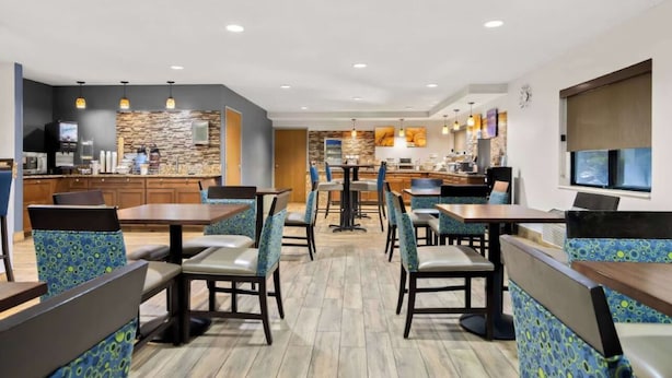 Un restaurant moderne avec des banquettes et des tables, un espace cuisine et un mur en pierres apparentes.