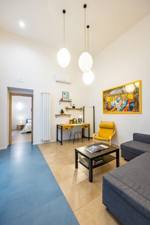 A modern living room with a sofa, a coffee table, a desk, and a chair. There is a painting on the wall and a door leading to another room. - Art Apartment by Napoliapartments (Naples)
