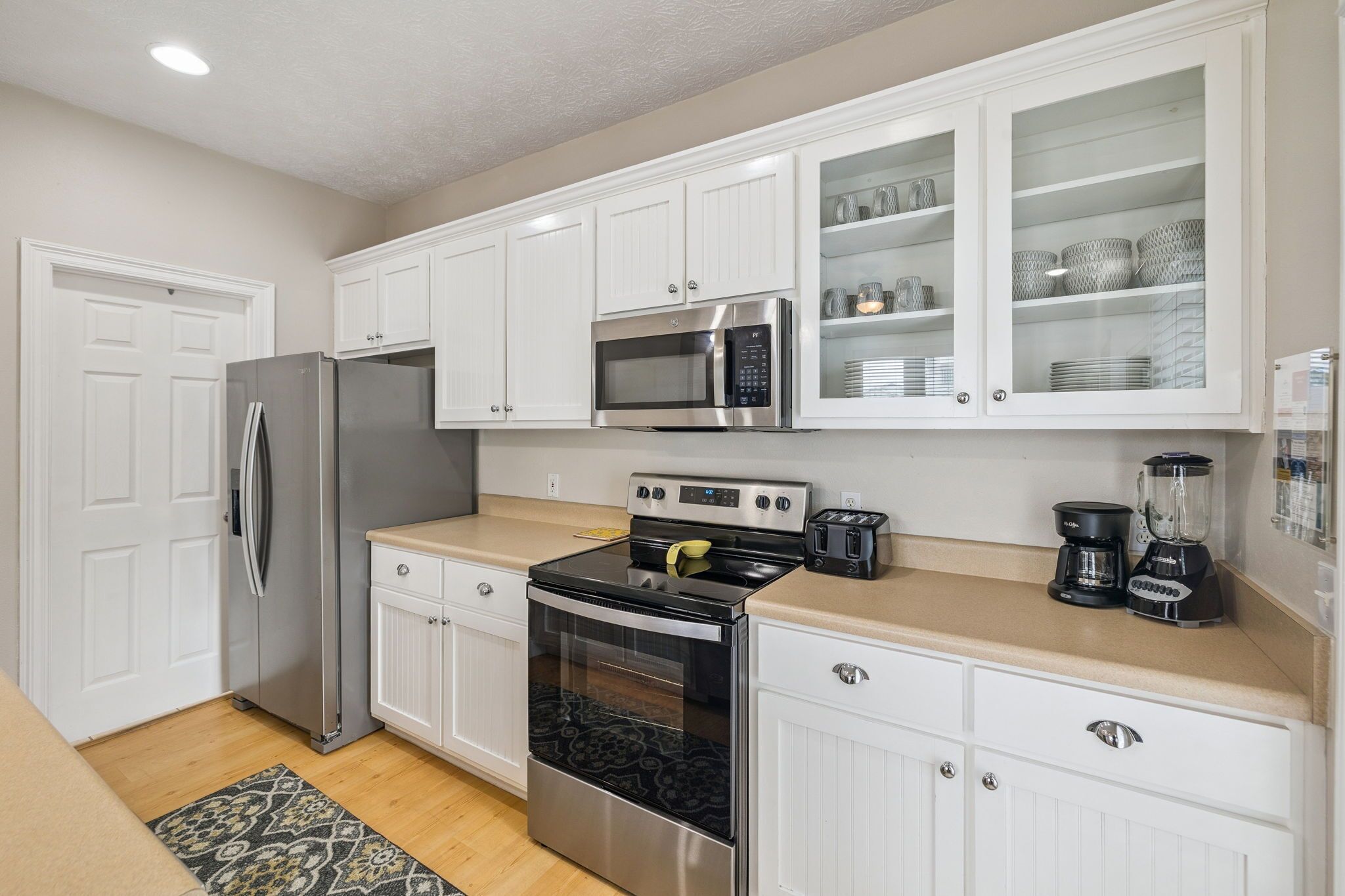 A kitchen with white cabinets, stainless steel appliances, a microwave, a coffee maker, and a blender.