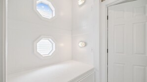 Una habitación con paredes blancas, un banco blanco y dos ventanas octagonales con tragaluces.