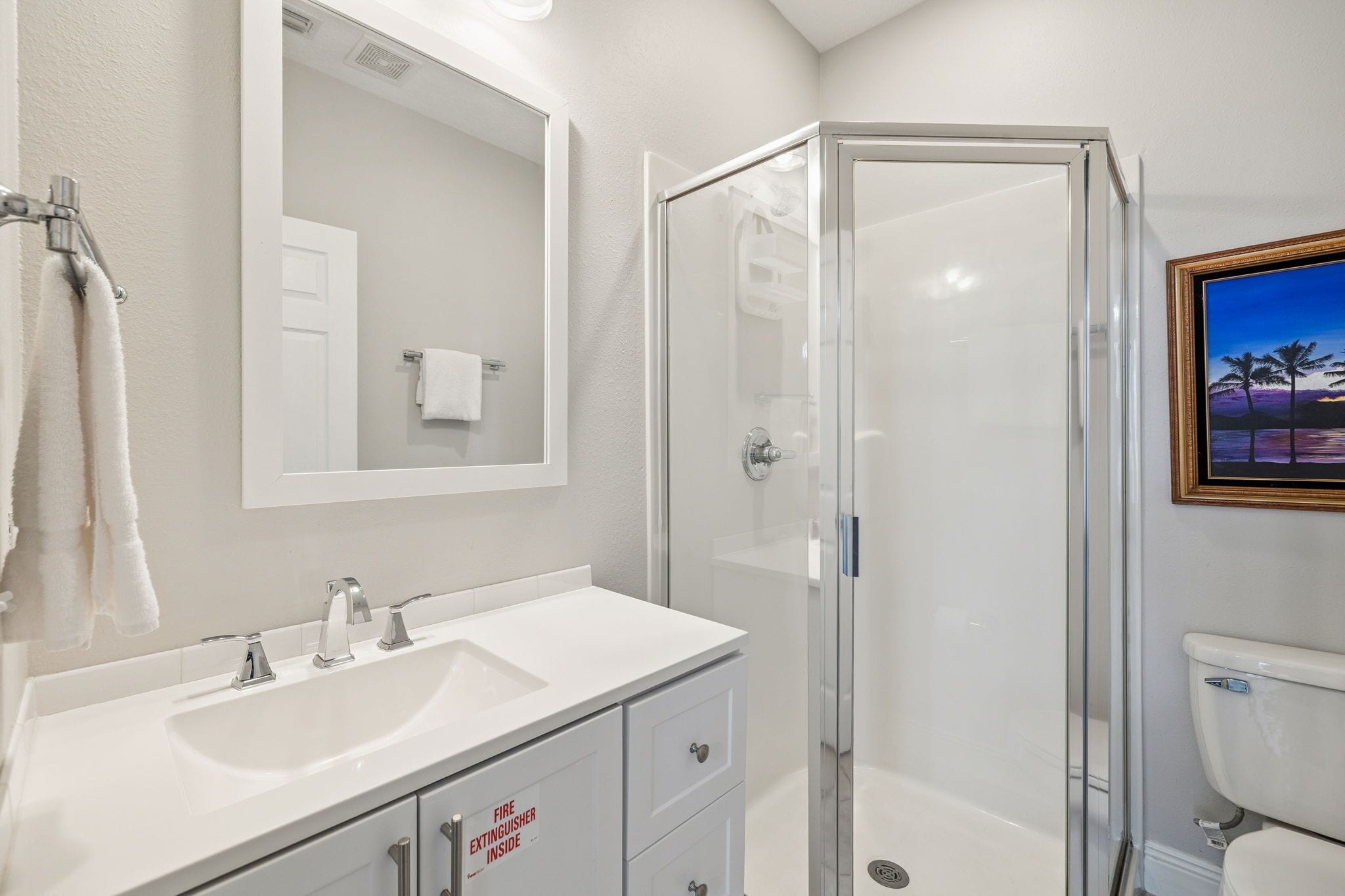 A modern bathroom with a white vanity, a glass shower enclosure, and a framed picture on the wall.