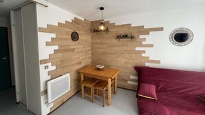 A compact room with a wooden wall design, a small wooden table, a red couch, and a mirror on the wall. - Bright T2 with mountain view and comfort (La Salle-les-Alpes)