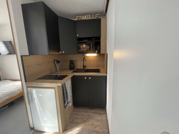 A compact kitchen with a refrigerator, sink, and wooden cabinets.