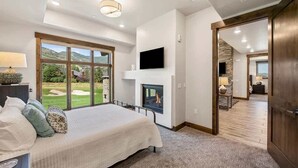 Ein Schlafzimmer mit einem großen Bett, einem Kamin, einem Fernseher und Blick ins Freie.