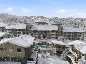 A snow-covered resort with multiple buildings, a central pool, and surrounding snowy mountains. - Powder Inn: Lux Condo|Canyons Village|Mtn Views (Park City)
