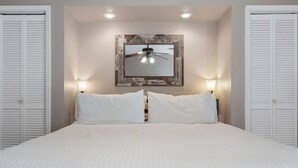 Un dormitorio con una cama grande, dos lámparas de noche, un ventilador de techo y casilleros blancos a cada lado.